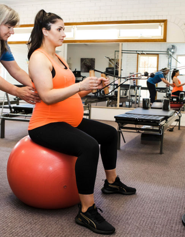 Exercise rehab in pregnancy, woman on a ball doing a row exercise on the cable